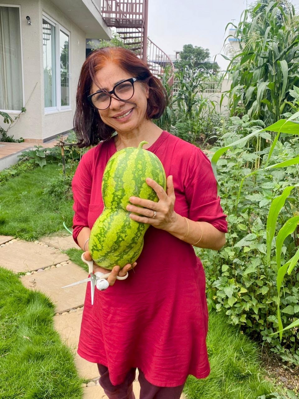 Mom smiling with a watermelon grown in Amatā's kitchen garden